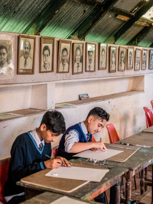 A pupil drawing in the art room beneath portraits of former Grahamites